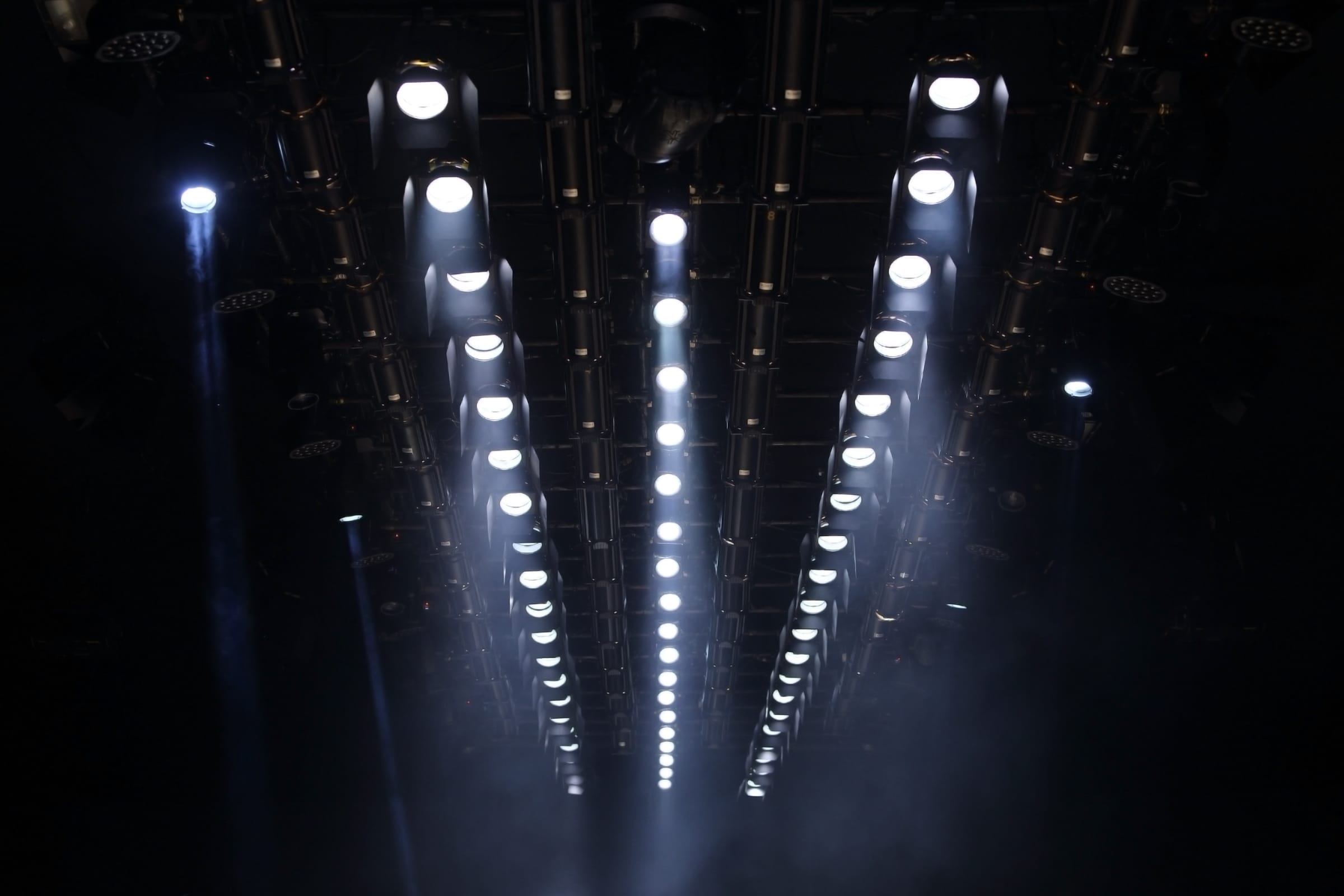 A rig of stage lights burning in the dark, beams cutting through haze.