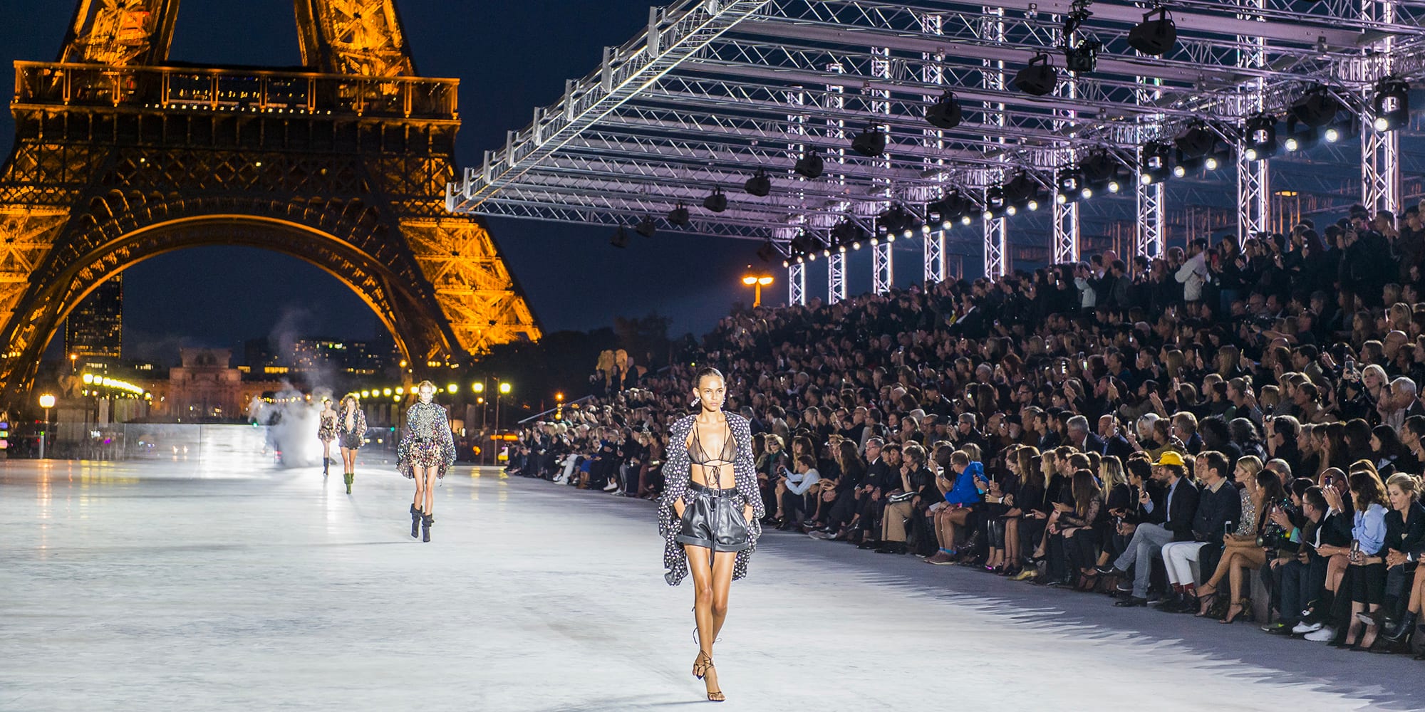 A night runway show at the Trocadéro, the Eiffel Tower lit, the front row at the edge of the catwalk.